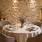 table ronde de restaurant dresser pour 4 personnes avec des chaises en tissu blanc, fond en pierre et bouquet de lavande