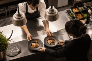 Le passe du restaurant, le cuisinier donne deux assiettes à la serveuse