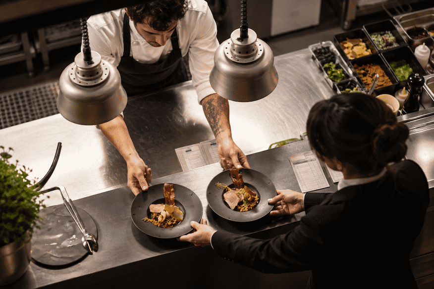 Le passe du restaurant, le cuisinier donne deux assiettes à la serveuse