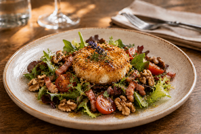 Salade de chèvre pané avec de la salade verte, des lardons, des tomates et des oignons.